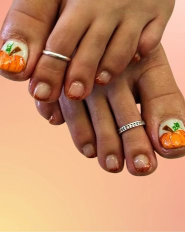 Toes with autumn-themed nail art featuring pumpkins and glittery tips.