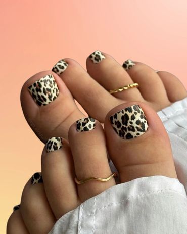 Feet with leopard print nail art and gold toe rings on a peach background in beauty salon