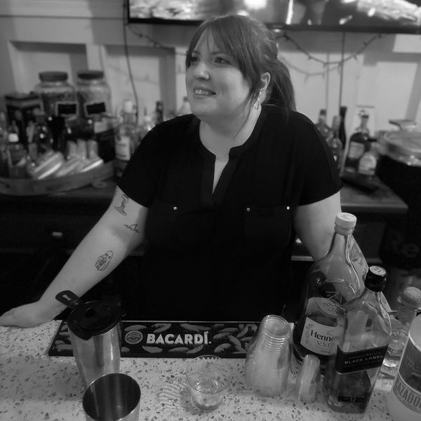 Jamie leaning on bar smiling behind an assortment of bottles