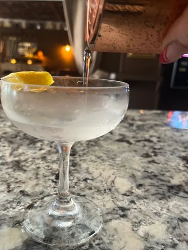 Manicured hand pores clear liquid into a frosty coupe glass