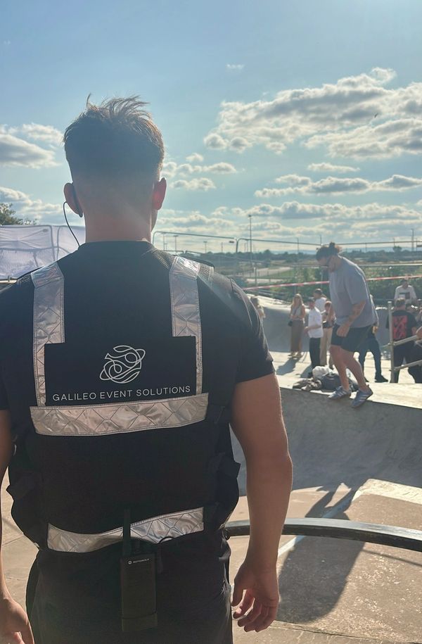A Galileo Event Solutions security staff member wearing a reflective vest stands near a skate park