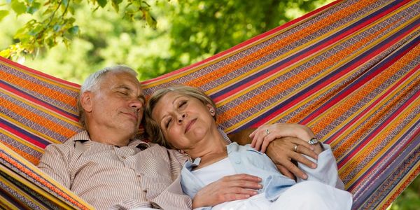 Elderly couple resting peacefully together on a colorful hammock outdoors.
