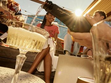 Friends enjoying a sunny day, pouring sparkling wine into a glass outdoors.