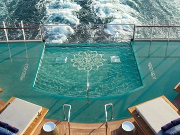View of a small pool on a ship's deck with ocean waves behind.