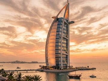 Sunset view of Burj Al Arab with illuminated pathway and beach scene.