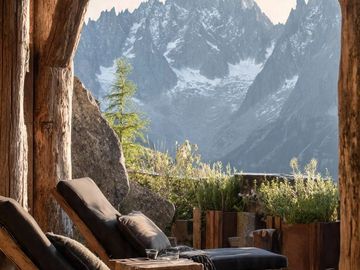 Cozy lounge chairs on a wooden deck overlooking snow-capped mountains.