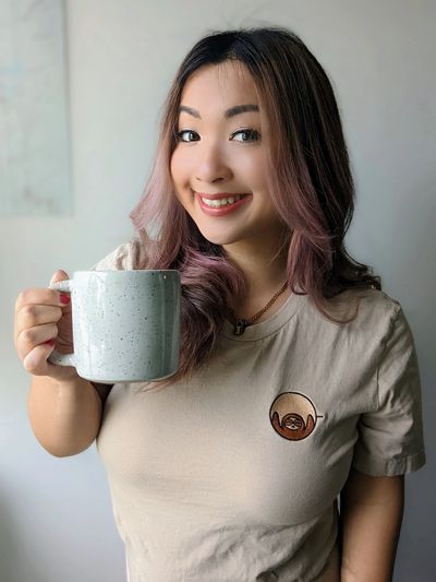 Photo of Jessica Lui, the face behind Slothee Coffee, smiling and holding a largeceramic coffee cup.