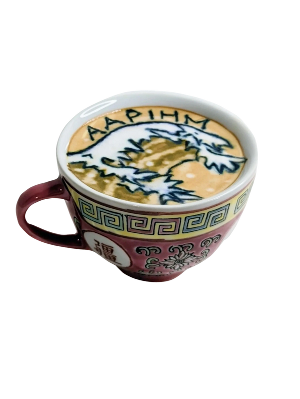 Top down side shot of a Chinese porcelain tea cup filled with a latte. A wave + AAPIHM written on it