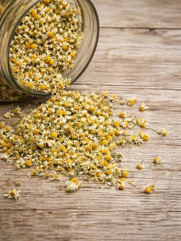 Dried chamomile flowers spilled from a glass jar onto a wooden surface.
