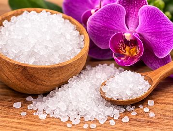 Coarse sea salt in a wooden bowl and spoon with a purple orchid flower.