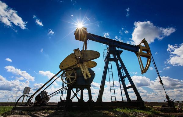 Oil pumpjack silhouette with bright sun and blue sky.