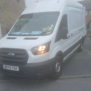 White Ford van parked on a residential street with headlights on.