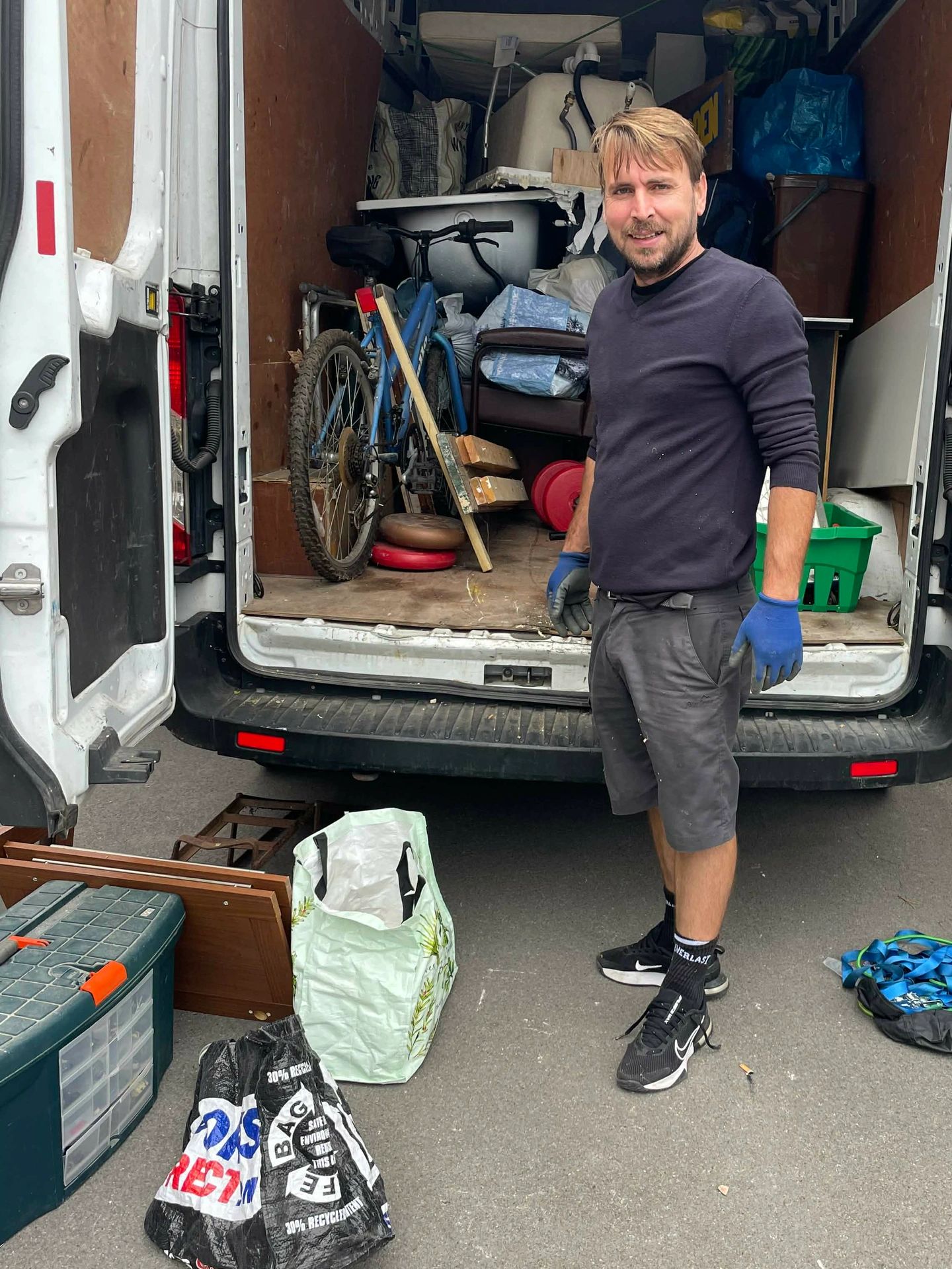 Man standing beside a van filled with various items and tools.