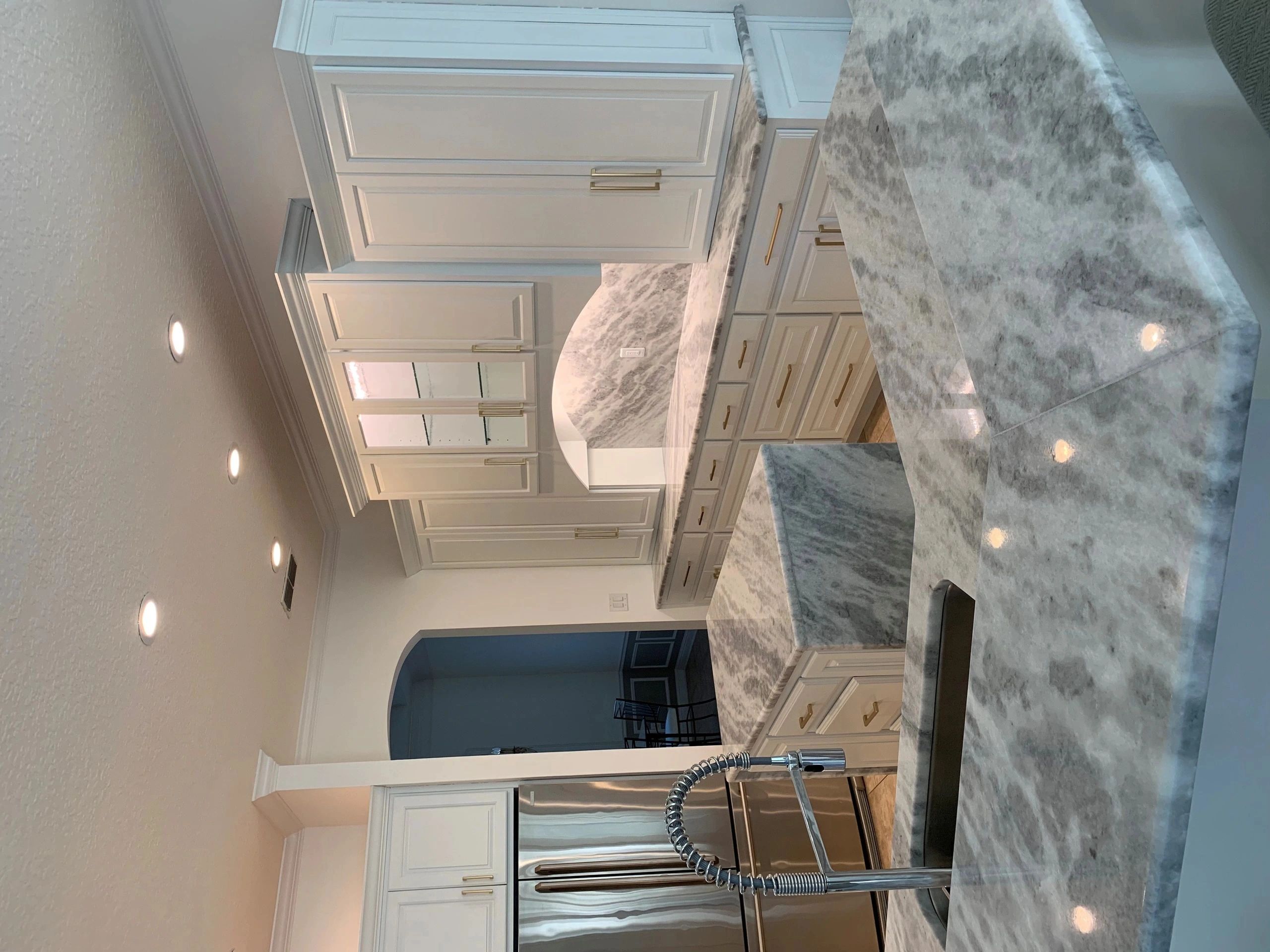 Modern kitchen with marble countertops and white cabinets.