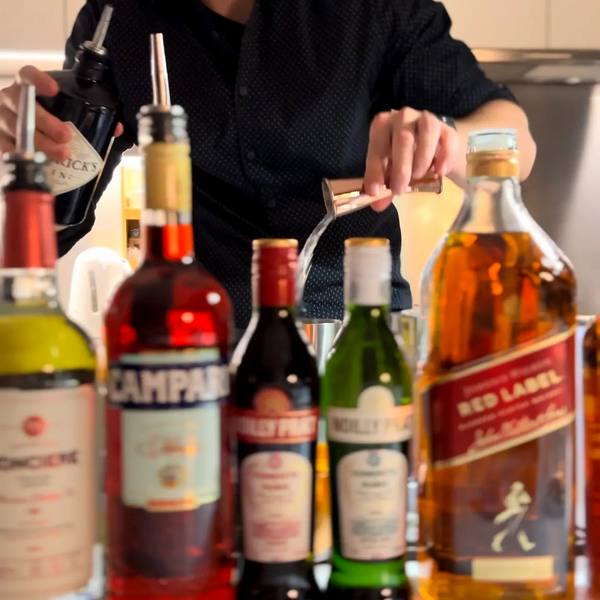 Bartender pouring a clear liquid with various liquor bottles in front.