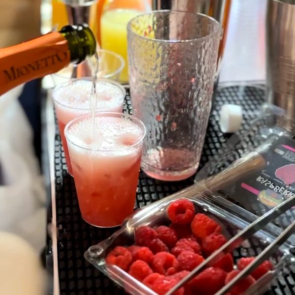 Pouring sparkling drink into raspberry cocktails with fresh raspberries nearby.