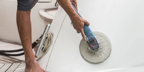 Person polishing a boat's white surface using a rotary polisher.