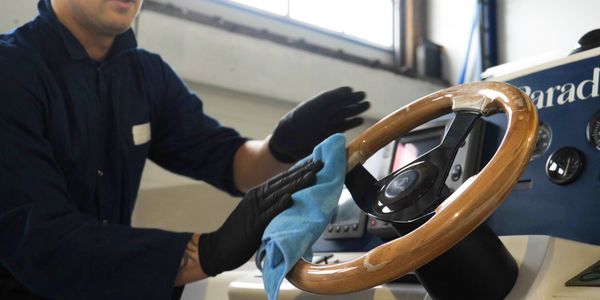 Person wearing gloves cleaning a wooden steering wheel with a blue cloth.