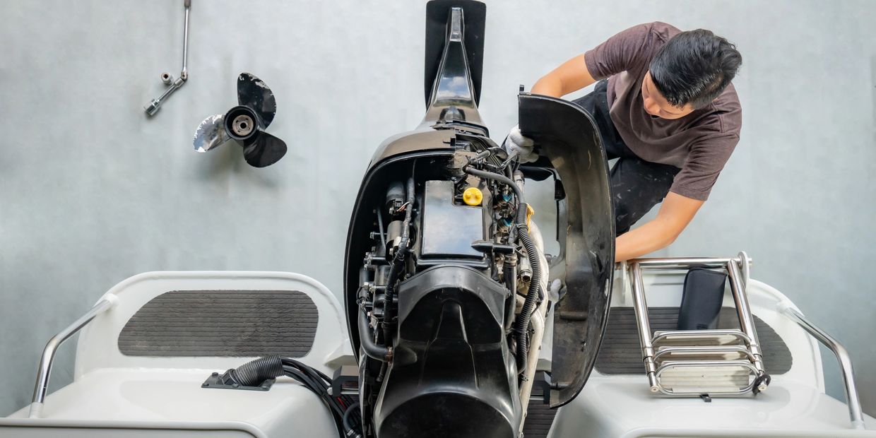A person repairing an outboard motor on a boat with tools nearby.