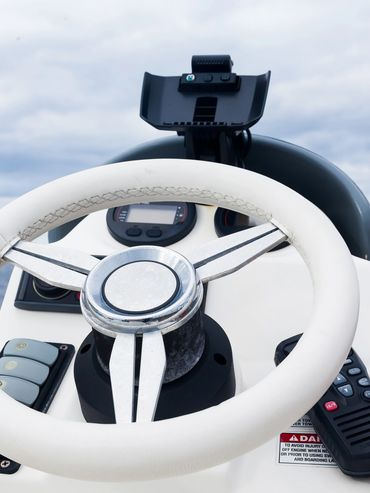 Close-up of a boat's steering wheel and control panel on open water.