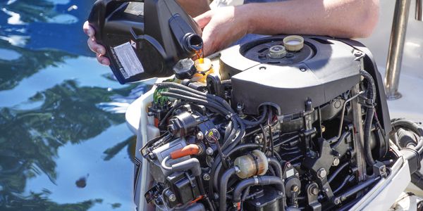 Person pouring oil into a boat engine near water.