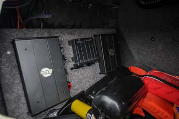 Three black electronic devices mounted on a grey carpeted surface with orange life jackets nearby.