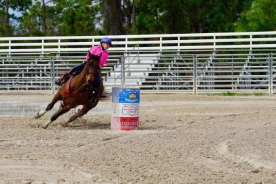 Rider in pink leans while horse makes a sharp turn around barrel.
