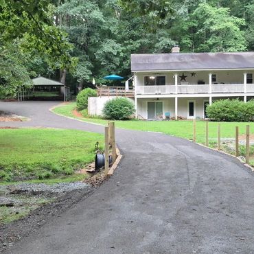 Country house with a long driveway surrounded by greenery and trees.