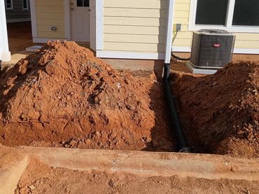 Two drainage pipes extending from a house with piles of dirt beside them.