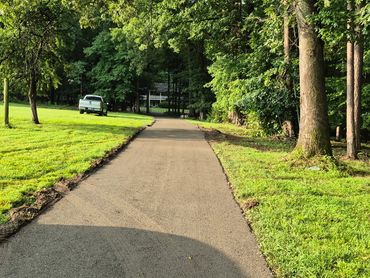 ABC stoned driveway leading to house surrounded by green lawns and trees.