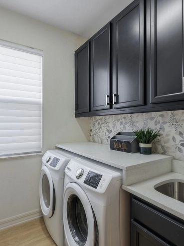 Modern laundry room with black cabinets and white appliances.