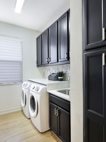 Modern laundry room with black cabinets, white washer and dryer, and wooden floor.