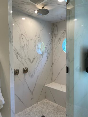Modern marble shower with built-in bench and round window.