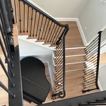 Top view of a wooden staircase with black railings around a grand piano below.