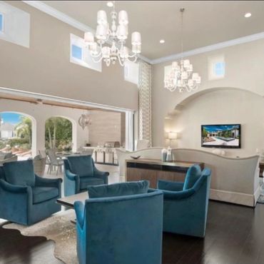 Spacious living room with blue armchairs and large windows overlooking a patio.