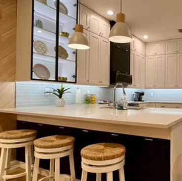 Modern kitchen with white cabinetry, hanging lights, and three wooden stools at the island.