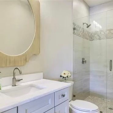 Modern bathroom with glass shower and large round mirror.