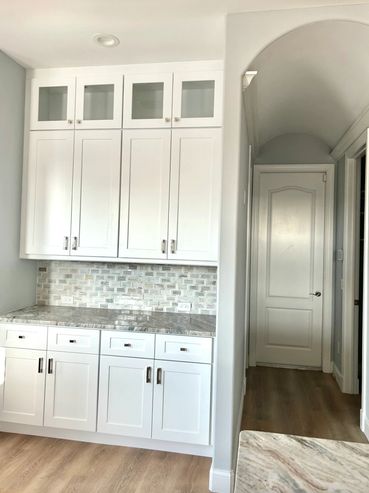 Modern white kitchen cabinets with marble countertops and a tiled backsplash.