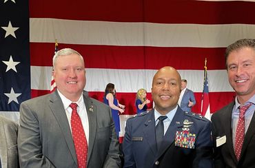 Four men in formal attire posing in front of a large American flag.