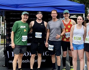 Group of six runners posing before a race under a blue tent.