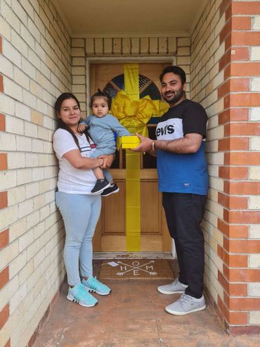 A family exchanging a yellow gift in front of a decorated door with a yellow ribbon.