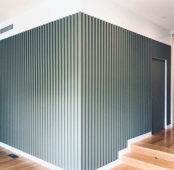 Modern interior corner wall with vertical green paneling and wooden flooring.