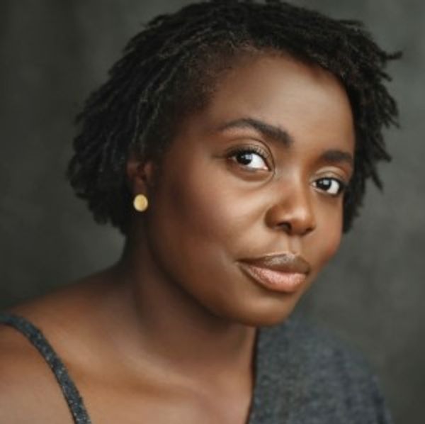 A confident woman with short natural hair and gold earrings.
