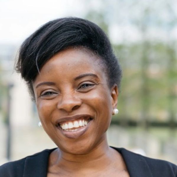 Smiling woman with natural hair and pearl earrings outdoors.