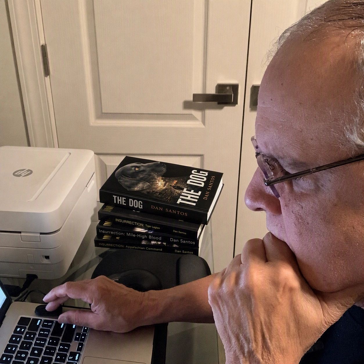 Man working on laptop near books and printer.