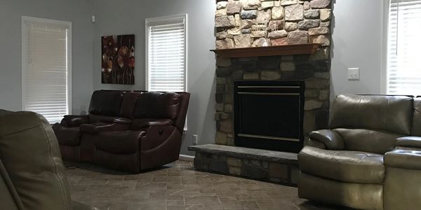 A family room with leather couches, a stone fireplace, and a black ceiling fan.