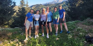 Group of six people posing outdoors with trees and mountains in the background.