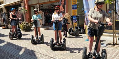 Group of people riding Segways on a cobblestone street in sunny weather.