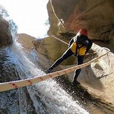 Person rappelling down a rocky waterfall using ropes and safety gear.