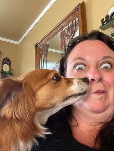 Dog affectionately nuzzles a woman's cheek inside a cozy home.